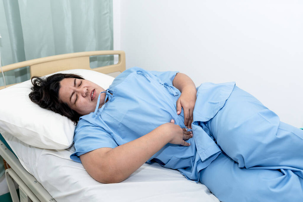 Aasialaisilla lihavilla naispotilailla, jotka makasivat potilaan sängyssä, hänellä oli voimakasta vatsakipua gastriitista ja suolitulehduksesta ihmisiin ja terveydenhuollon käsitteeseen.. - Valokuva, kuva