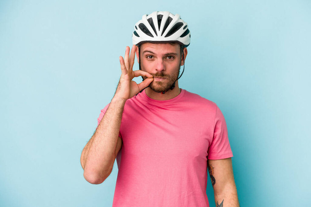 Jeune homme caucasien avec casque de vélo isolé sur fond bleu avec les doigts sur les lèvres gardant un secret. - Photo, image