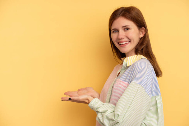 Young English woman isolated on yellow background holding a copy space on a palm. - Fotoğraf, Görsel