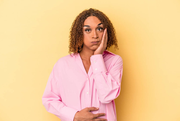 Young latin transsexual woman isolated on yellow background blows cheeks, has tired expression. Facial expression concept. - Fotó, kép