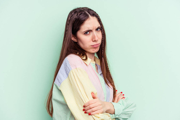 Young caucasian woman isolated on green background frowning face in displeasure, keeps arms folded. - Фото, изображение