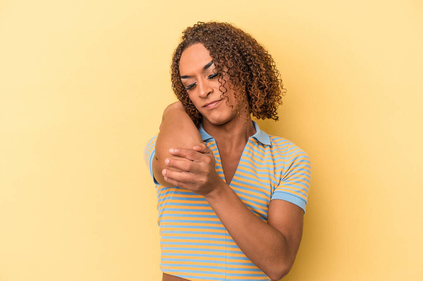 Junge lateinamerikanische transsexuelle Frau isoliert auf gelbem Hintergrund massiert Ellbogen, leidet nach einer schlechten Bewegung. - Foto, Bild
