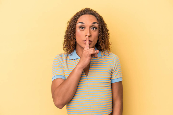 Giovane donna transessuale latina isolata su sfondo giallo mantenendo un segreto o chiedendo silenzio. - Foto, immagini