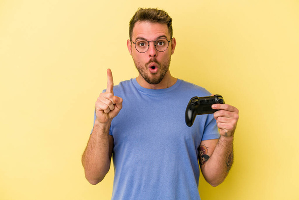 Young caucasian man holding a game controller isolated on yellow background having some great idea, concept of creativity. - Fotoğraf, Görsel