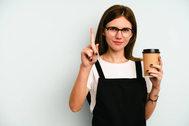 Restaurant waiter woman holding a take away coffee isolated on blue background showing number one with finger. - Foto, immagini
