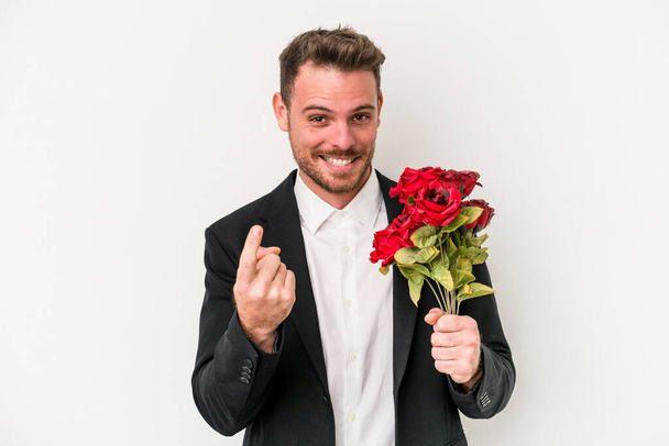 Young caucasian man holding bouquet of flowers isolated on white background pointing with finger at you as if inviting come closer. - 写真・画像