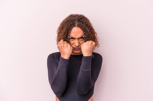 Young latin transsexual woman isolated on pink background throwing a punch, anger, fighting due to an argument, boxing. - Фото, изображение