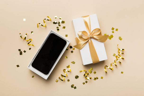 Boîte cadeau ouverte avec ruban or et smartphone sur fond couleur, vue de dessus. Modèle d'emballage de boîte ouverte vierge, modèle pour votre conception - maquette de marque. - Photo, image