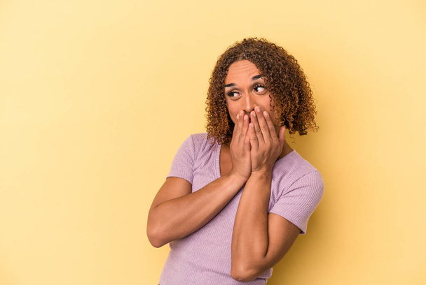 Young latin transsexual woman isolated on yellow background laughing about something, covering mouth with hands. - 写真・画像