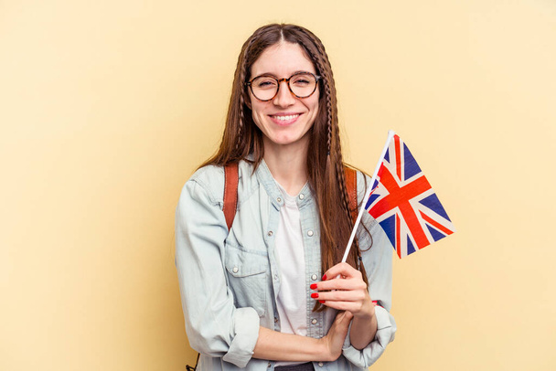Junge kaukasische Frau studiert Englisch isoliert auf gelbem Hintergrund, lacht und hat Spaß. - Foto, Bild