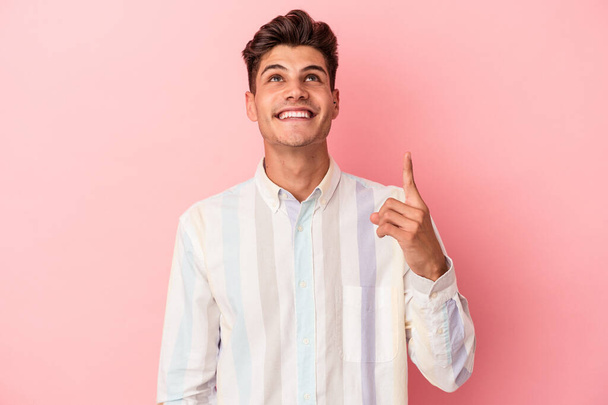 Giovane uomo caucasico isolato su sfondo rosa indica con entrambe le dita anteriori in alto mostrando uno spazio vuoto. - Foto, immagini