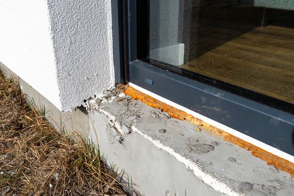 Старая пожелтевшая монтажная пена под большим окном террасы, видимый пенопласт, изолирующий фундамент дома. - Фото, изображение