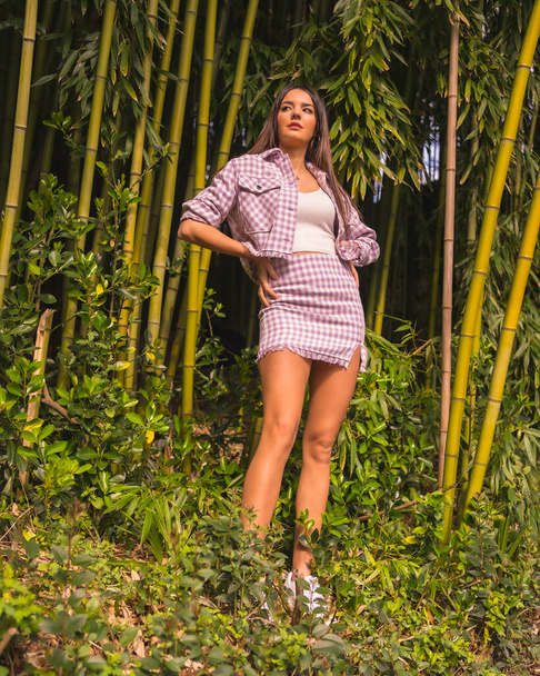 Young caucasian girl with a pink skirt in a bamboo forest. Enjoying the city on summer vacation in a tropical climate, a young girl lifestyle - Zdjęcie, obraz