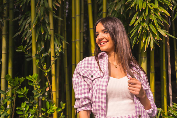 Young caucasian girl with a pink skirt in a bamboo forest. Enjoying the city on summer vacation in a tropical climate, lifestyle of a young girl smiling - Photo, image