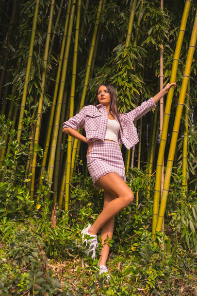 Young caucasian girl with a pink skirt in a bamboo forest. Enjoying the city on summer vacation in a tropical climate, lifestyle of a young girl in a trendy posing - Zdjęcie, obraz