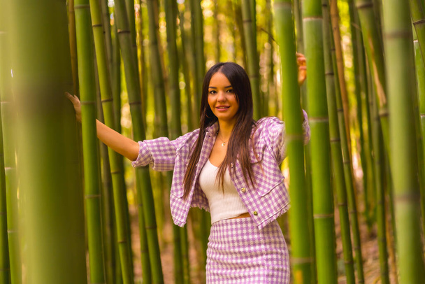Young caucasian girl with a pink skirt in a bamboo forest. Enjoying the city on summer vacation in a tropical climate, a girl lifestyle walking and smiling in the forest - Foto, afbeelding