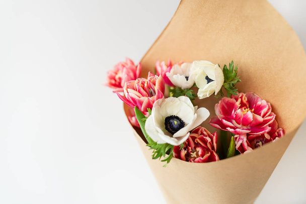 Beautiful red and white bouquet of tulips and anemones in kraft paper. The concept of spring and flowering. With copy space - Photo, Image