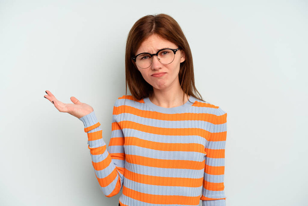 Young English woman isolated on blue background doubting and shrugging shoulders in questioning gesture. - Photo, Image