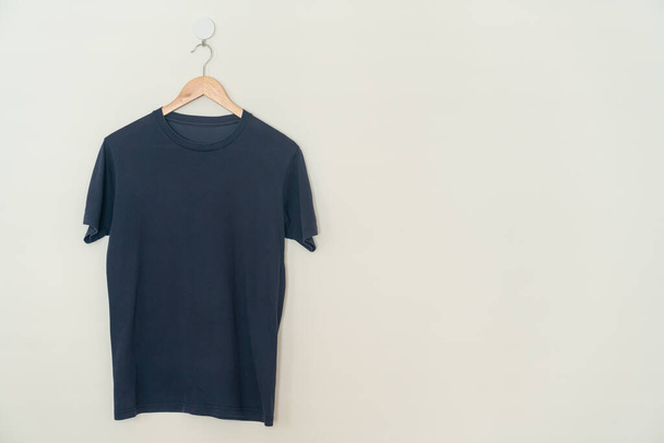 navy t-shirt hanging with wood hanger on wall - Zdjęcie, obraz