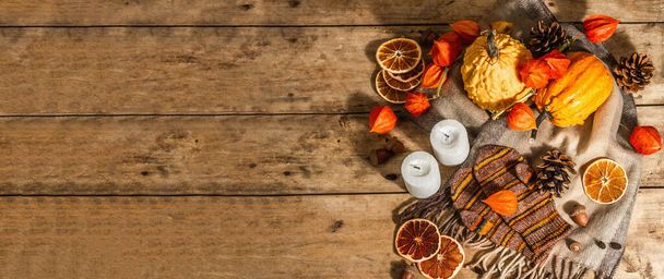 Autumn cozy composition. Scarf, warm mittens, candles, pumpkins, fall decor. Wooden rustic background, banner format - Photo, Image