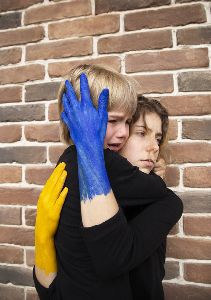 Síró fiú és egy sárga-kék festett kezű fiatal nő ölelkeznek. Család, támogatás, tapasztalat, kétségbeesés érzései. Gondoskodunk egymásról az ukrajnai háború alatt. - Fotó, kép