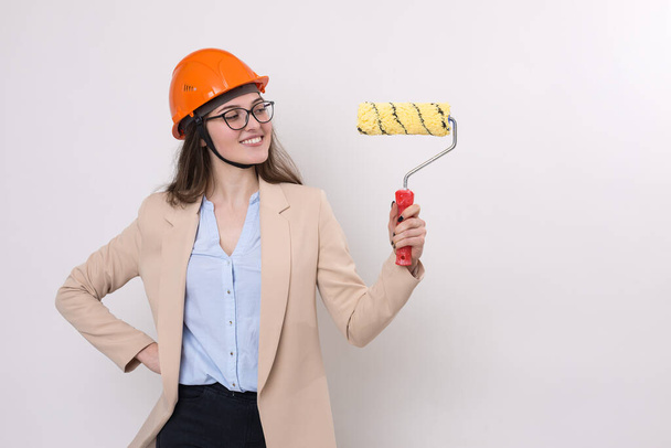 Girl engineer in an orange construction helmet with plastering painting tools in her hands on a white background. - Foto, Imagem