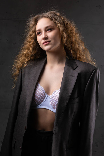 Portrait of a young red-haired curly sexy girl in a jacket with long hair in the studio. Dramatic photo in dark colors. - Φωτογραφία, εικόνα