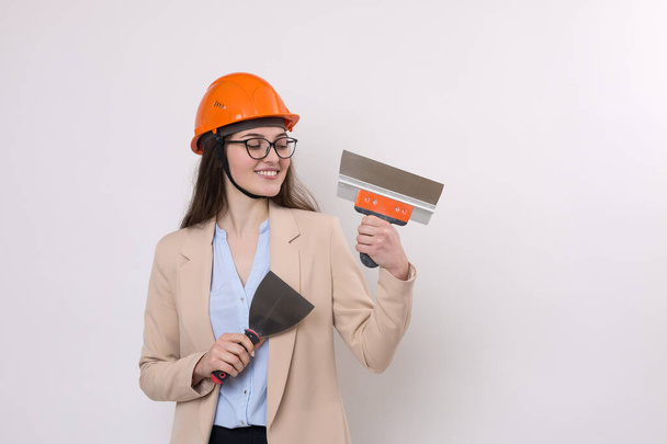 Girl engineer in an orange construction helmet with plastering painting tools in her hands on a white background. - Photo, Image