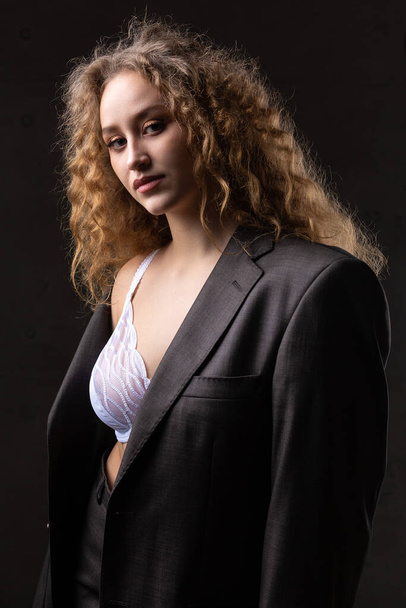 Портрет молодої рудої кучерявої сексуальної дівчини в піджаку з довгим волоссям в студії. Драматична фотографія в темних тонах
. - Фото, зображення