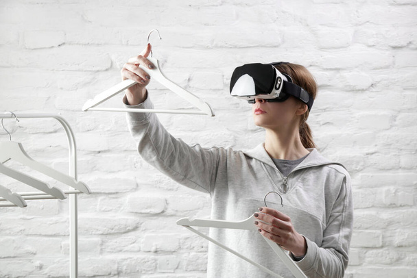 Portret kobiety w okularach VR wybierającej strój z wieszaka na ubrania. Doświadczenie wirtualnej rzeczywistości i koncepcja przyszłej technologii.  - Zdjęcie, obraz
