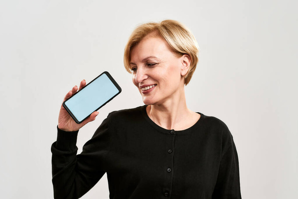 Smiling woman showing and looking at smartphone - Valokuva, kuva