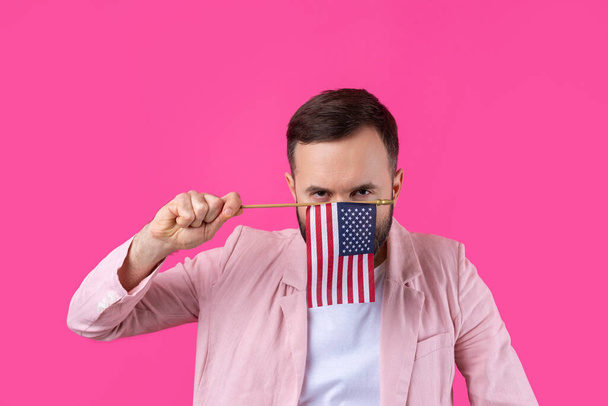 Egy elégedett fiatalember portréja, szakállal, amerikai zászlóval, vörös stúdió háttérrel. Nagy amerikai hazafi és a szabadság védelmezője. - Fotó, kép