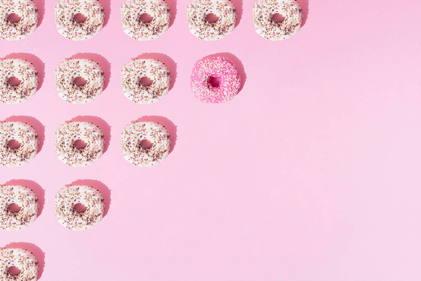 Arranged ring donuts like a triangle with white and pink glaze and colorful crumbs on a pink pastel background. Copy space and pattern. - Foto, afbeelding