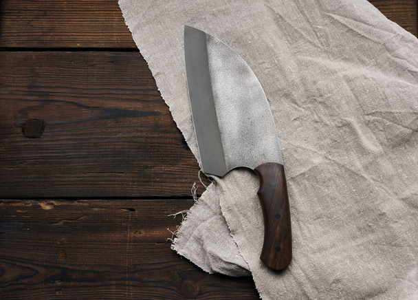 μεταλλικό κοφτερό μαχαίρι κουζίνας σε ξύλινη λαβή σε καφέ τραπέζι από σανίδες, πάνω όψη - Φωτογραφία, εικόνα