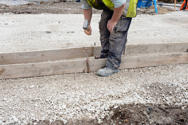Travailleur au sol faisant obturateur pour béton pour former une base pour le trottoir à l'aide de planches d'échafaudage et épingles de route en acier lors de la construction de nouvelles routes - Photo, image