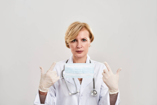 Mature female doctor hold and show medical mask - 写真・画像