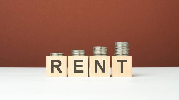 word rent on wooden blocks in brown background with increasing stack of coins - Photo, Image