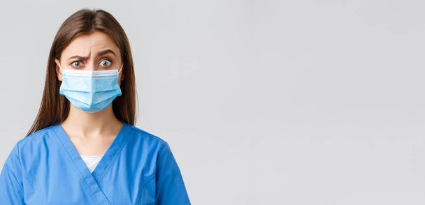 Ковид-19, профилактика вируса, здоровье, медицинские работники и карантин. Привлекательная женщина-врач или медсестра в клинике, в синем халате и медицинской маске, выглядит скептически или подозрительно
 - Фото, изображение