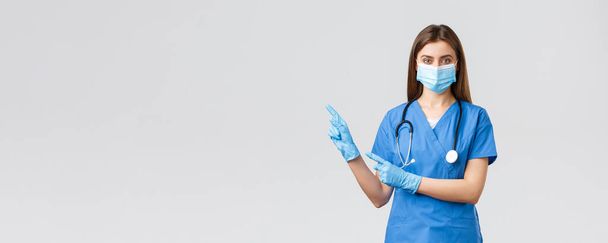 Covid-19 、ウイルス、健康、医療従事者および検疫の概念を防止する。青のスクラブで快適な女性医師や看護師,医療マスクと手袋,フォローページやクリックリンクを招待,左を指して - 写真・画像