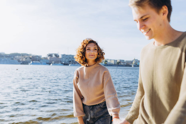 two young people in love running on the beach. They smile at each other. Beautiful couple holding hands. Beach. Feeling. Dress in a sweater - Photo, Image