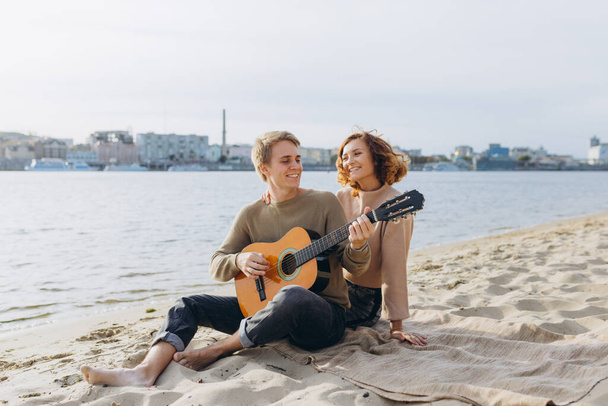 Happy couple in love. Stunning sensual portrait of a young couple. Young man playing guitar for his beloved girl. - Photo, Image