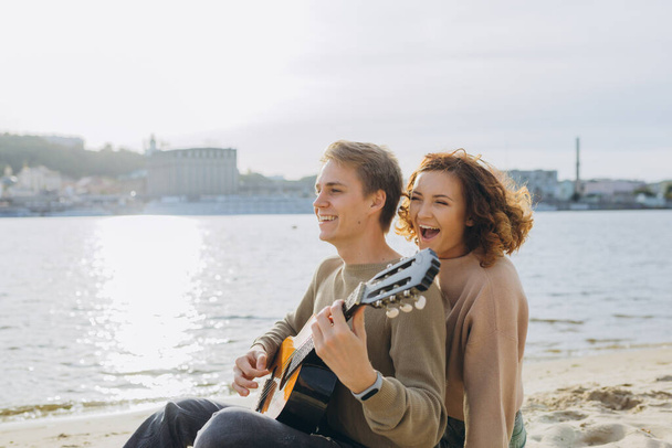 Glückliches verliebtes Paar. Atemberaubend sinnliches Porträt eines jungen Paares. Junger Mann spielt Gitarre für sein geliebtes Mädchen. - Foto, Bild