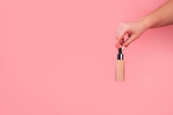 Foundation with a female hand on a pink background. BB cream for professional make-up, eyedropper for applying to the face. Cosmetic female accessory, liquid fluid. Mock up concept - Photo, image