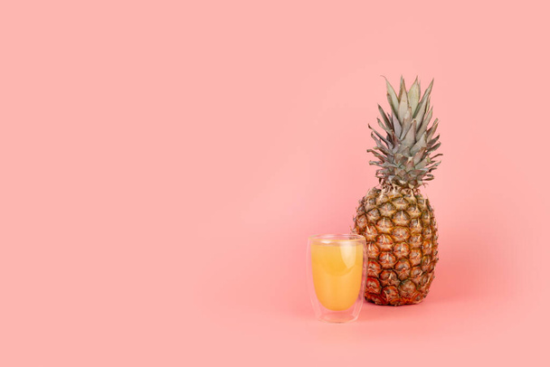 Ananas und ein Glas Ananassaft auf isoliertem pastellrosa Hintergrund mit Copyspace. Minimales Fruchtkonzept. Ernährungskonzept - Foto, Bild