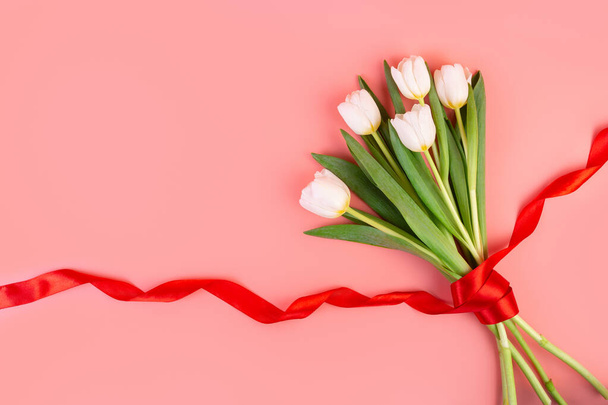 Weiße Tulpen blühen, flach. Schöner Strauß von Tulpen am Stiel mit Blättern isoliert auf pastellrosa Hintergrund. Natur-Designobjekt zum Frauentag, Muttertag, Jubiläum. Frühjahrskonzept - Foto, Bild