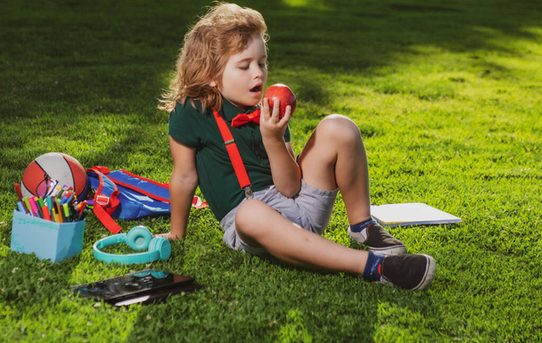 Kid sitting outdoor in garden eating apple. Lttle child outdoor school, education, on line distance learning. - 写真・画像