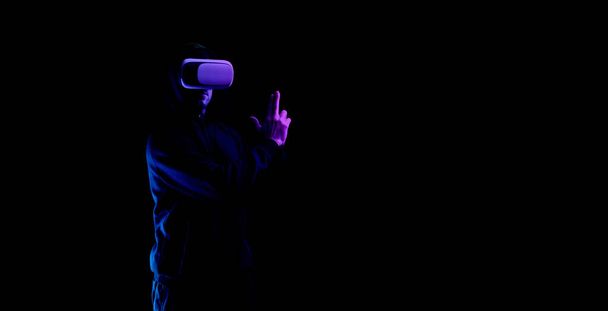 Vr goggles virtual reality. Young man in digital helmet for 3d virtual reality game isolated on black neon background. Study and virtual world in 3D simulation - Photo, Image