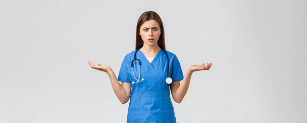 Healthcare workers, prevent virus, insurance and medicine concept. Confused and puzzled female nurse, doctor in blue scrubs, spread hands sideways and shrugging, cant understand - Photo, Image