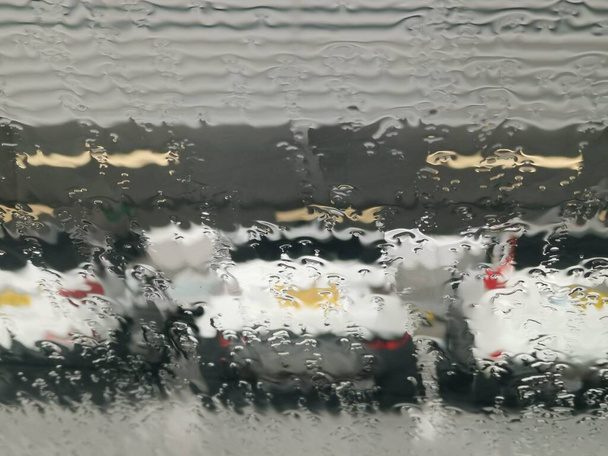 Vue floue des voitures stationnées à travers la fenêtre couverte de pluie - Photo, image