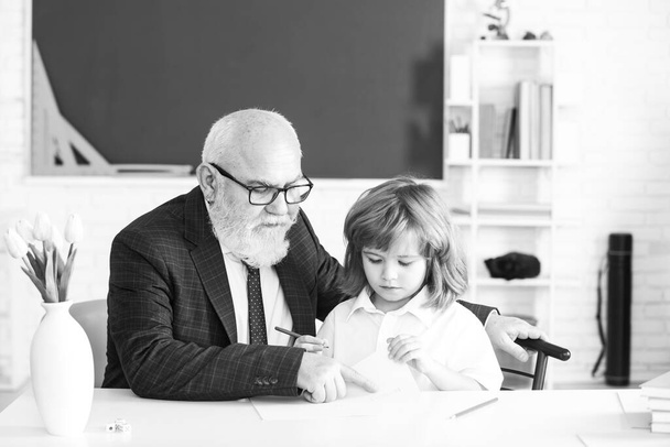 Elementary pupil reading and writing with teacher in classroom. Old senior teacher and school boy pupil. - Foto, Bild